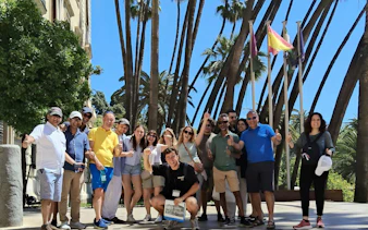 Tour group exploring Málaga with guide near palm trees and flags.