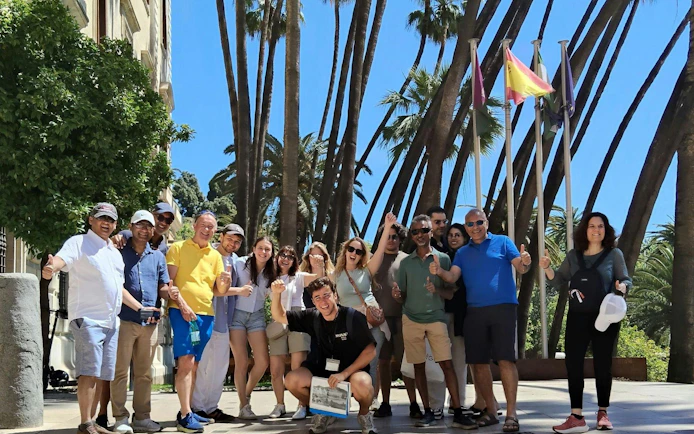 Tour group exploring Málaga with guide near palm trees and flags.
