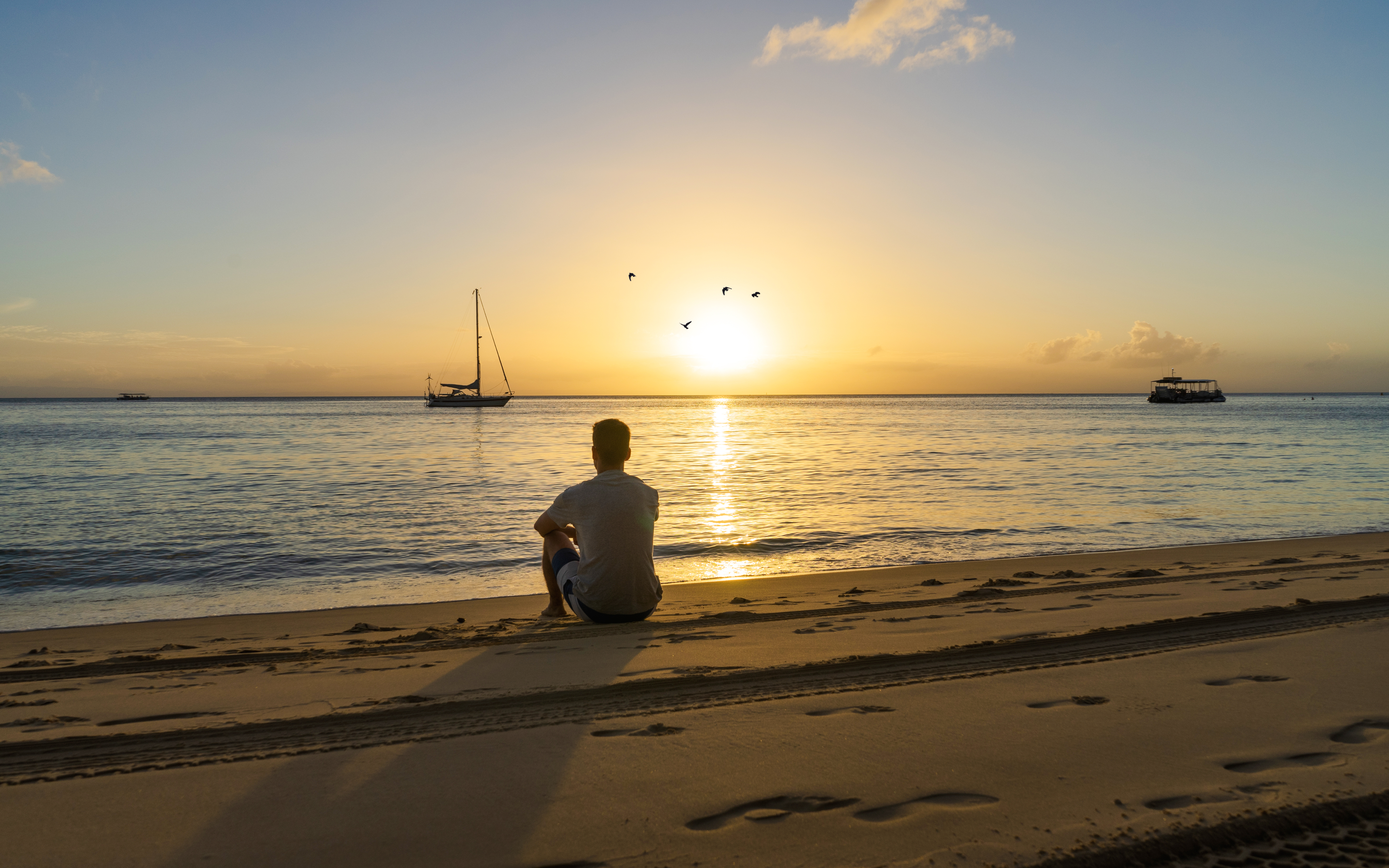 Sunset over Tangalooma Island shipwrecks with a person sitting on Moreton Island beach.