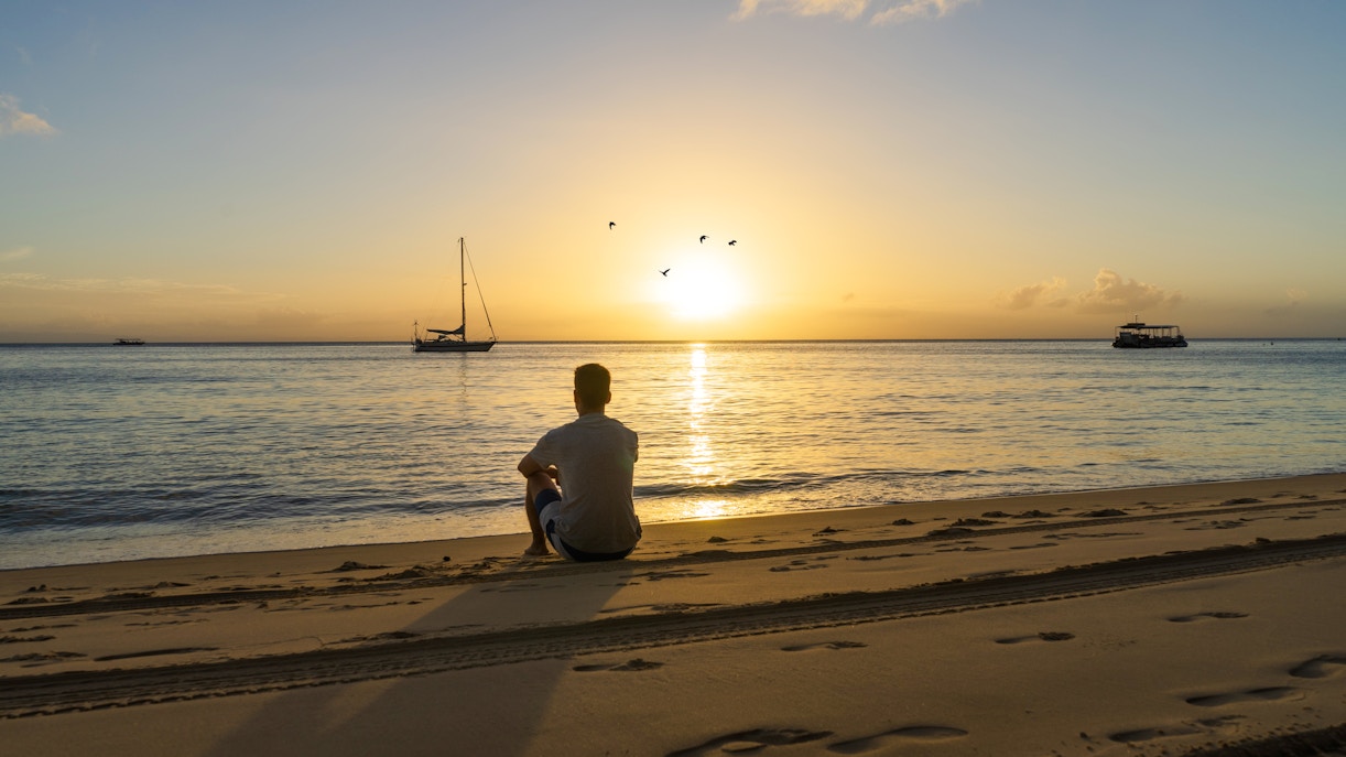 Sunset over Tangalooma Island shipwrecks with a person sitting on Moreton Island beach.