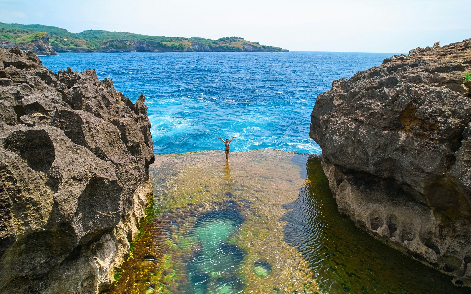 Group of tourists exploaring the beautiful West Nusa Penida Island with hotel transfers included, standing on a cliff overlooking the crystal clear ocean