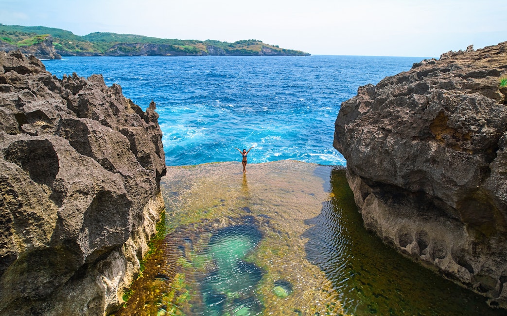 Tourist standing on a cliff at West Nusa Penida Island, overlooking the ocean.