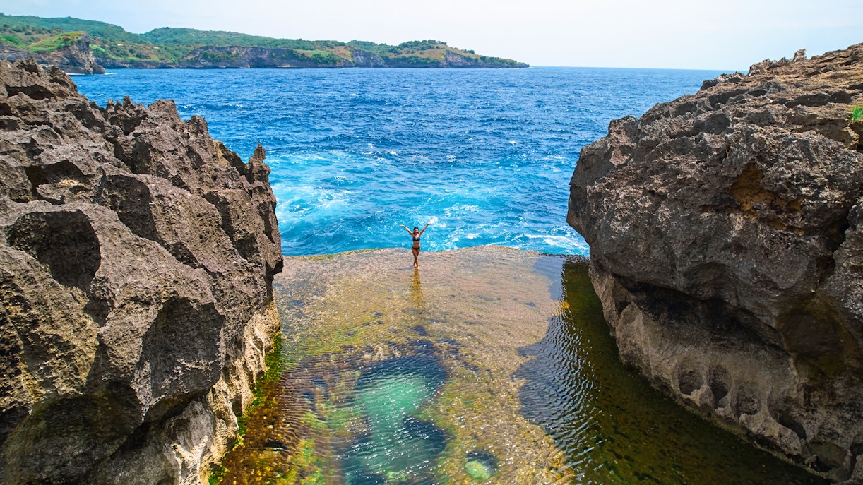 Group of tourists exploaring the beautiful West Nusa Penida Island with hotel transfers included, standing on a cliff overlooking the crystal clear ocean