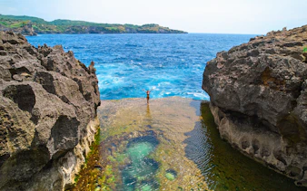 Tourist standing on a cliff at West Nusa Penida Island, overlooking the ocean.