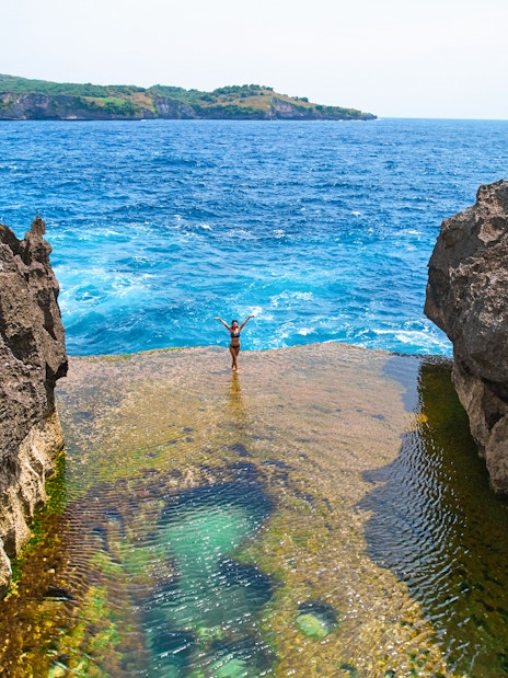 Tourist standing on a cliff at West Nusa Penida Island, overlooking the ocean.