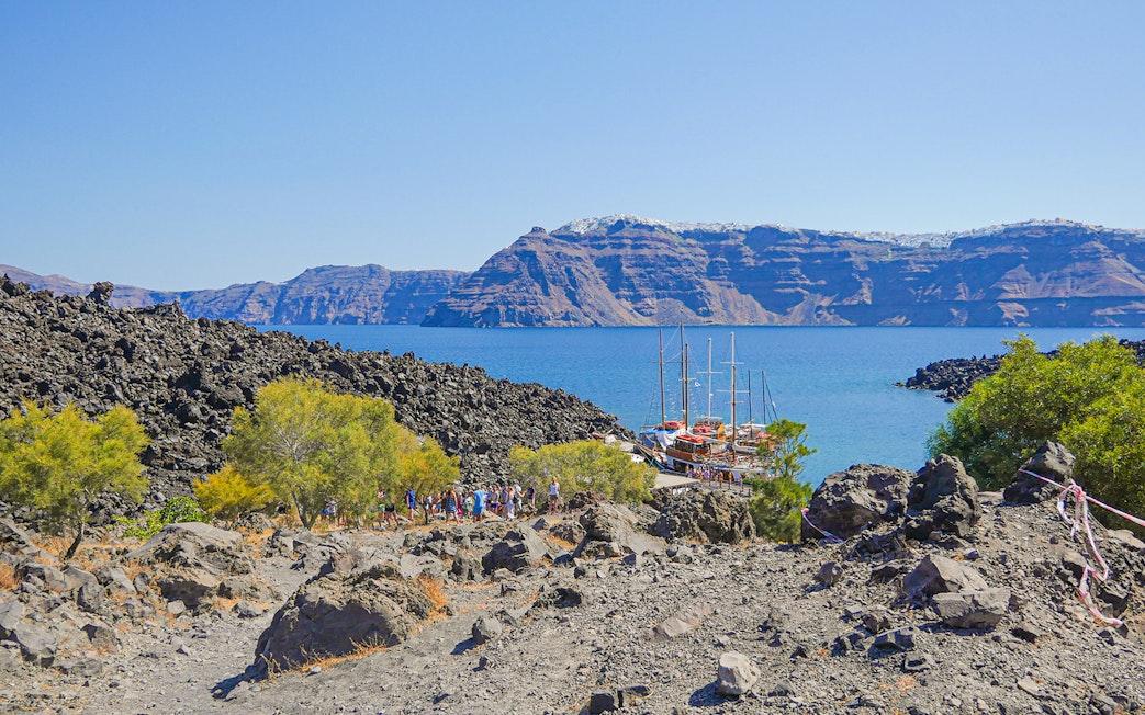 Santorini volcanic landscape with tourists hiking near docked boats.