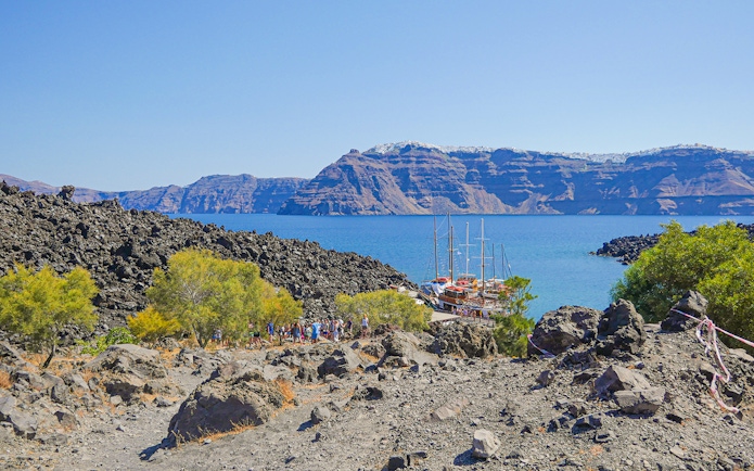 Santorini volcanic landscape with tourists hiking near docked boats.