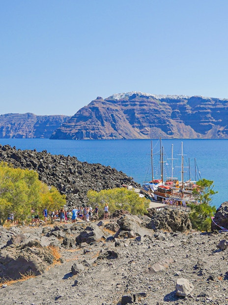 Santorini volcanic landscape with tourists hiking near docked boats.