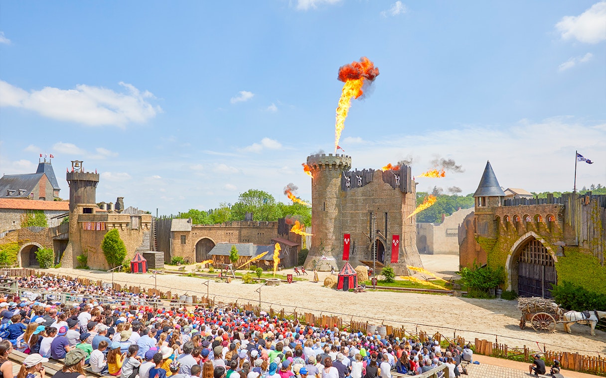 Crowd watching medieval castle show with fire effects at Puy du Fou, France.