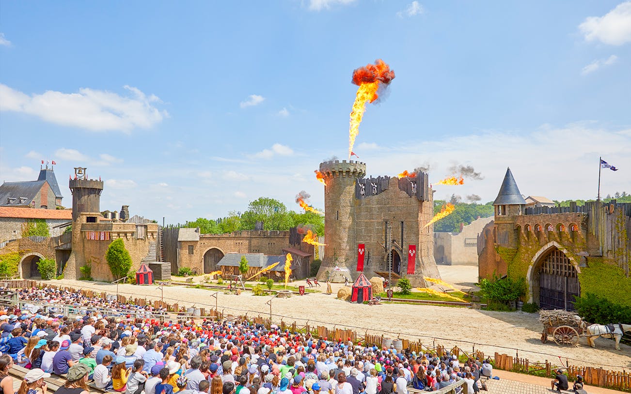 Crowd watching medieval castle show with fire effects at Puy du Fou, France.