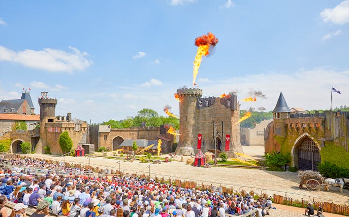 Crowd watching medieval castle show with fire effects at Puy du Fou, France.