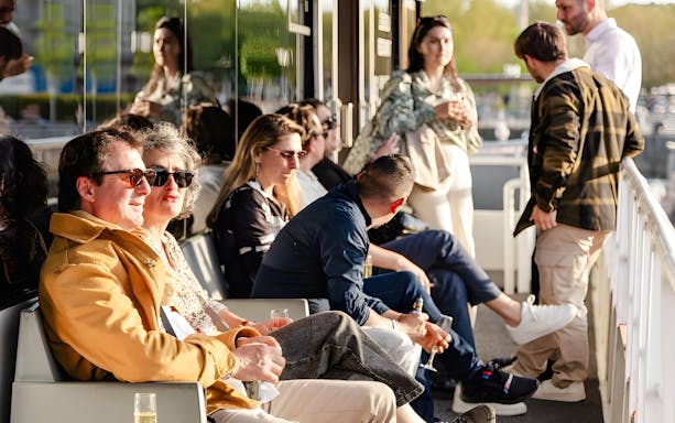 People enjoying a Bateaux Bordelais cruise, seated on a deck with drinks.