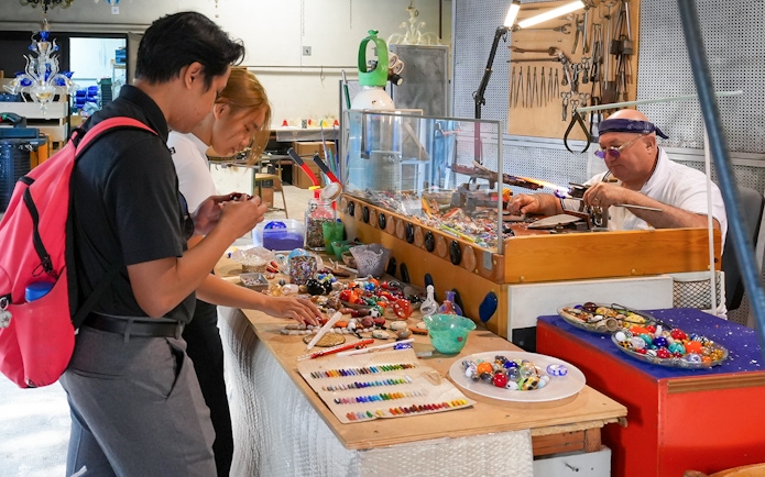 Glass artist crafting intricate pieces in a showroom as visitors observe.