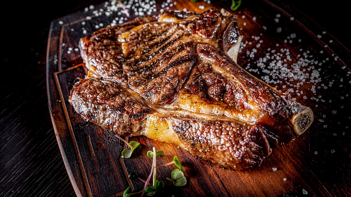 Steak on bones with salt on wooden board.
