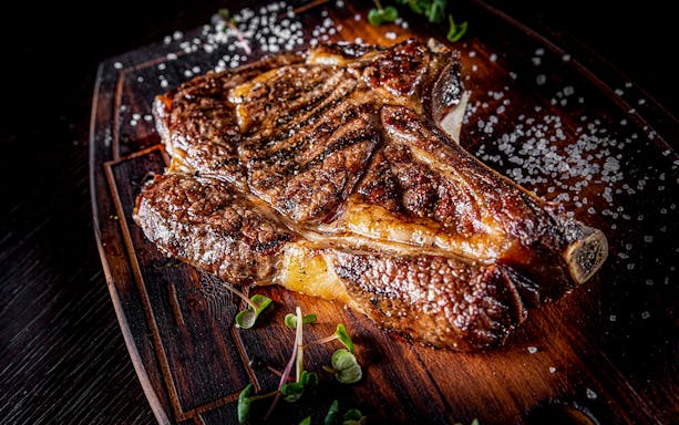 Steak on bones with salt on wooden board.