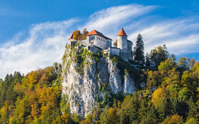 Bled Castle perched on a cliff surrounded by autumn trees, Slovenia.