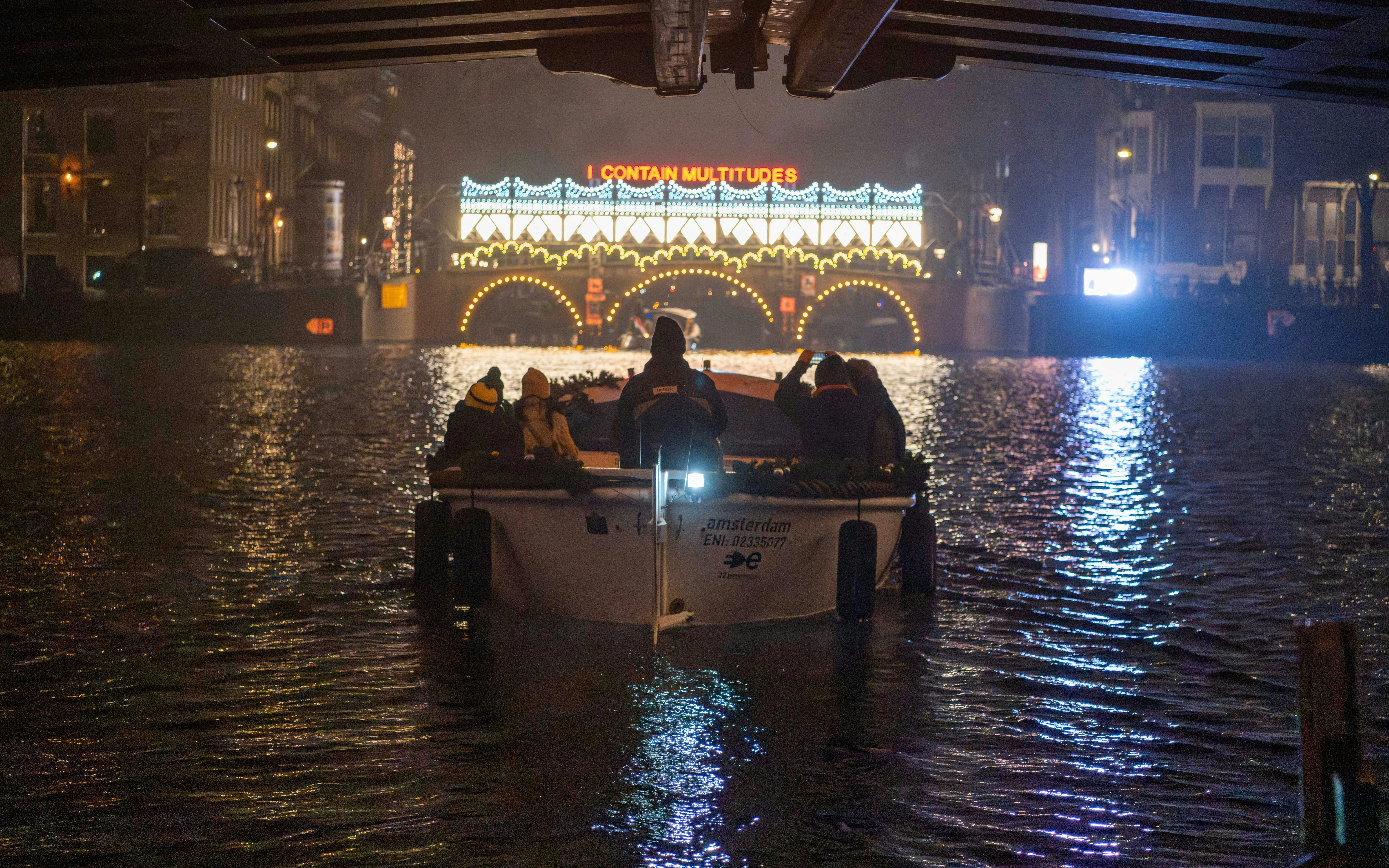 Boat tour under illuminated bridge at Amsterdam Light Festival.