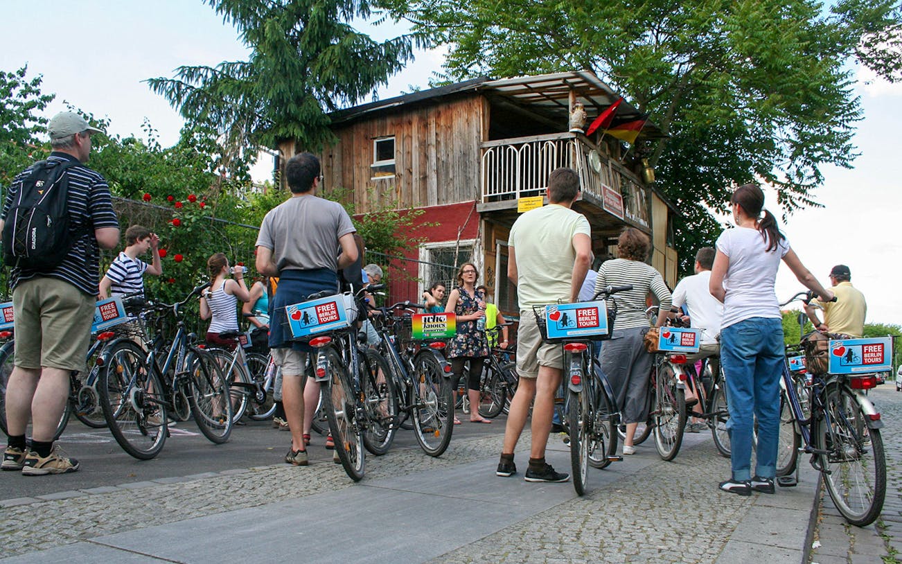 Group of cyclists on a guided bike tour in Berlin, stopping near a rustic wooden building.