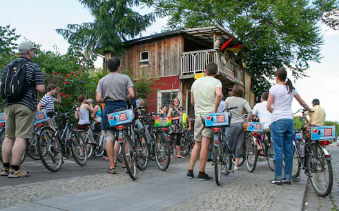 Group of cyclists on a guided bike tour in Berlin, stopping near a rustic wooden building.