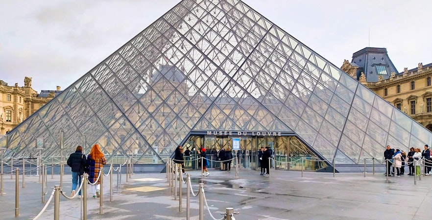 Louvre Pyramid entrance with visitors in Paris, France.
