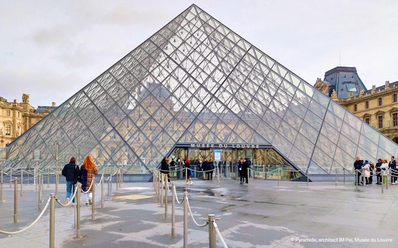 Louvre Pyramid entrance with visitors in Paris, France.