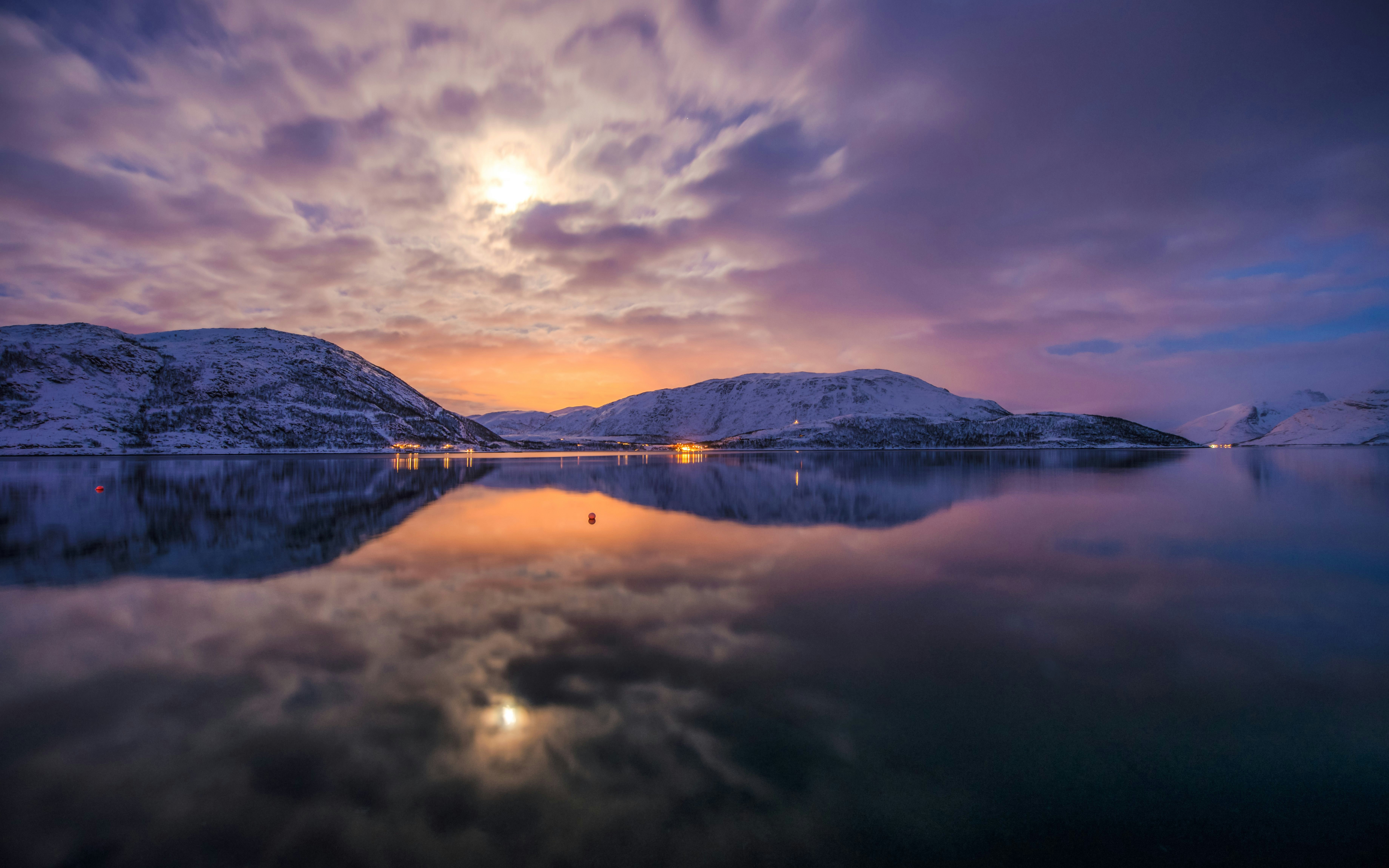 Snow-covered mountains reflecting in Skulsfjord under a moonlit sky.