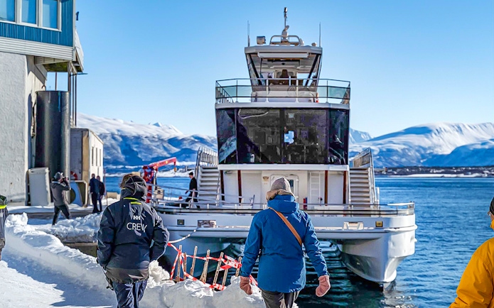 People boarding a boat in snowy Tromsø, Norway, with mountains in the background.