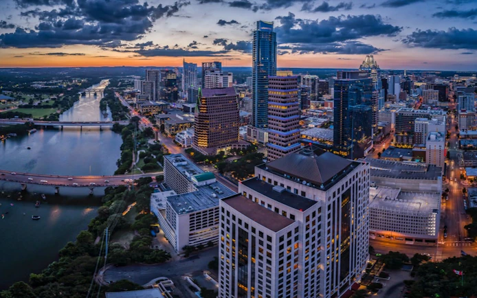Austin skyline at sunset with high-rise buildings and Lady Bird Lake, part of the Ghosts of Austin tour.