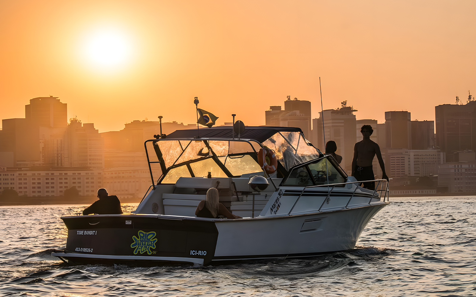 Tourists on a boat during Rio de Janeiro sunset cruise with city skyline in the background.