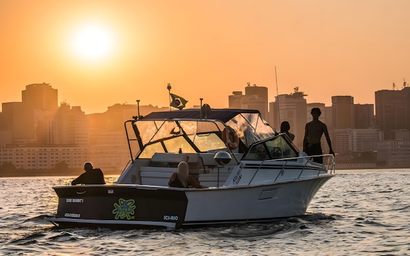 Tourists on a boat during Rio de Janeiro sunset cruise with city skyline in the background.