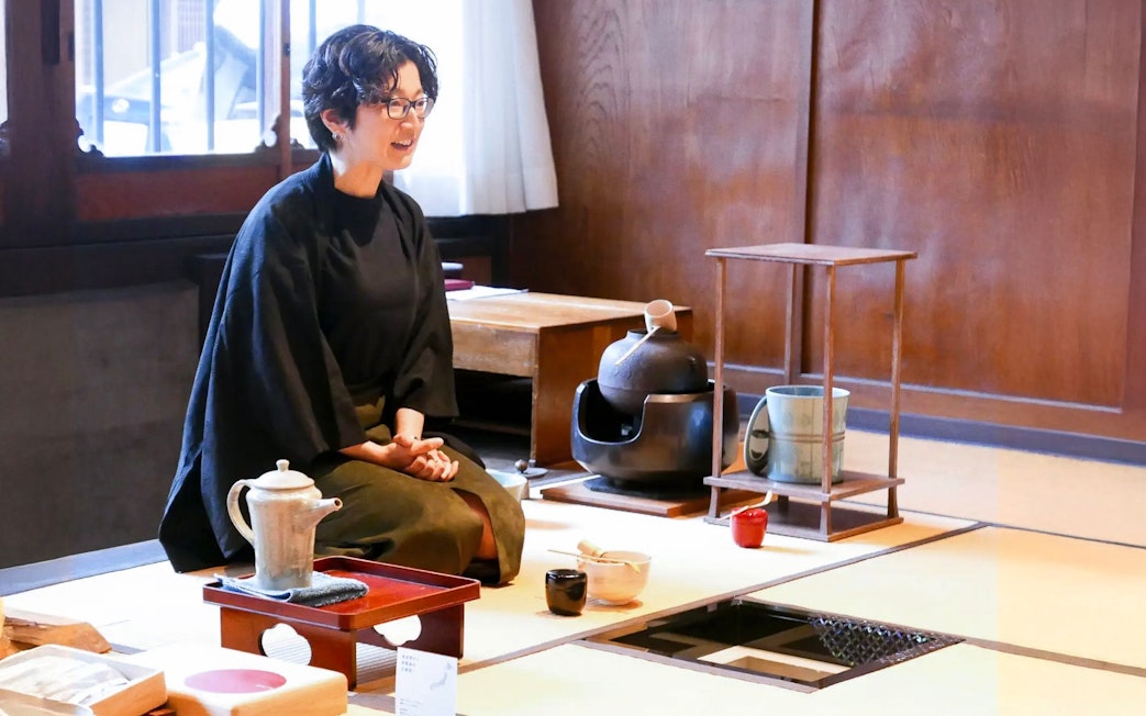 Guide demonstrating matcha making process in traditional Japanese tea room.