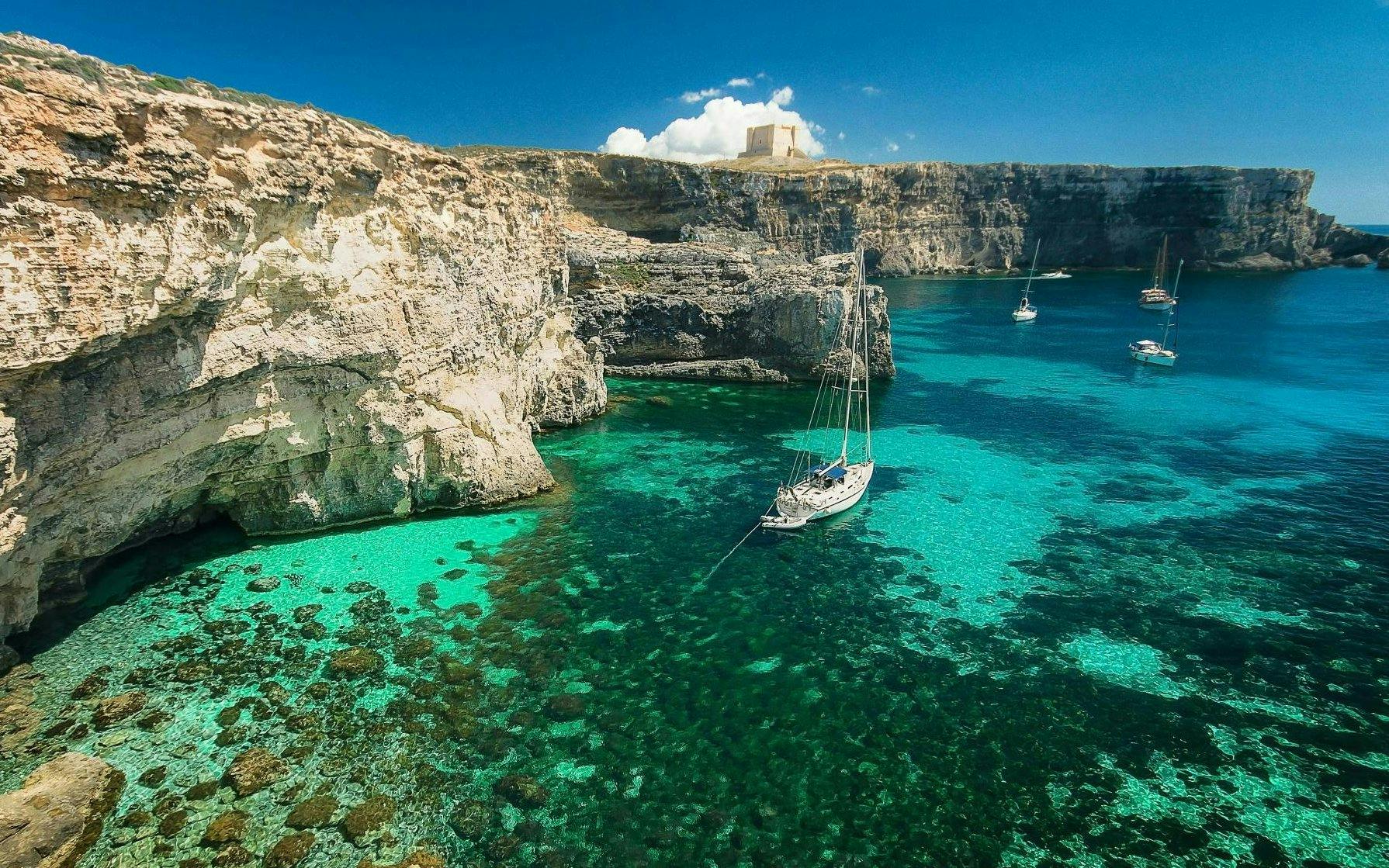 Sailboats in clear turquoise waters near cliffs at Blue Lagoon, Gozo.