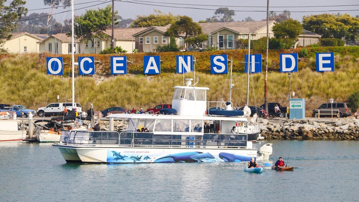 Whale watching boat in Oceanside Harbor, San Diego, with kayakers nearby.