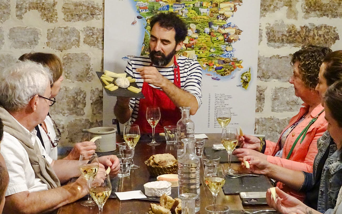 Expert discussing cheese varieties at Cheese Museum Paris, France with visitors seated around a table.