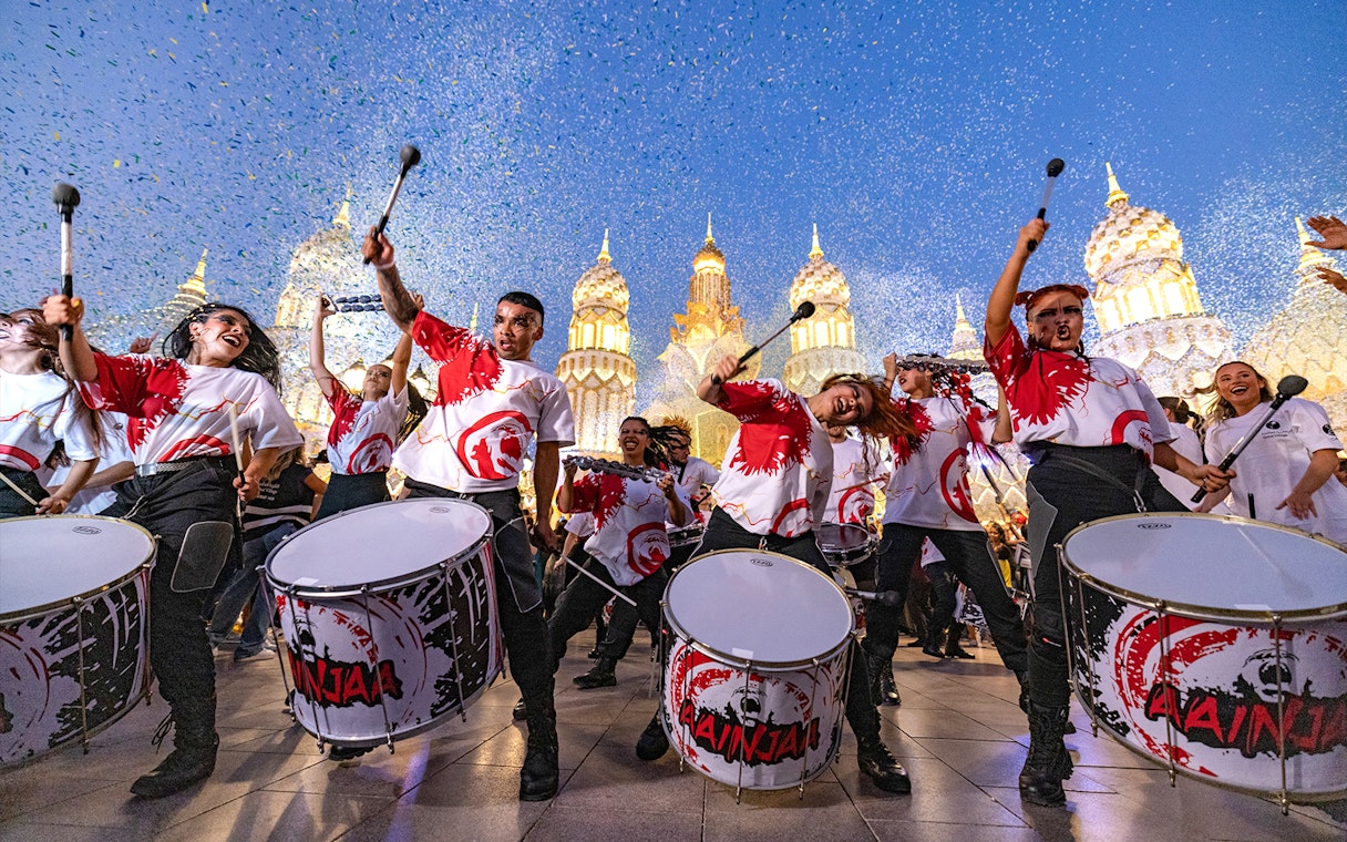 Drummers performing at Global Village Dubai with illuminated pavilions in the background.