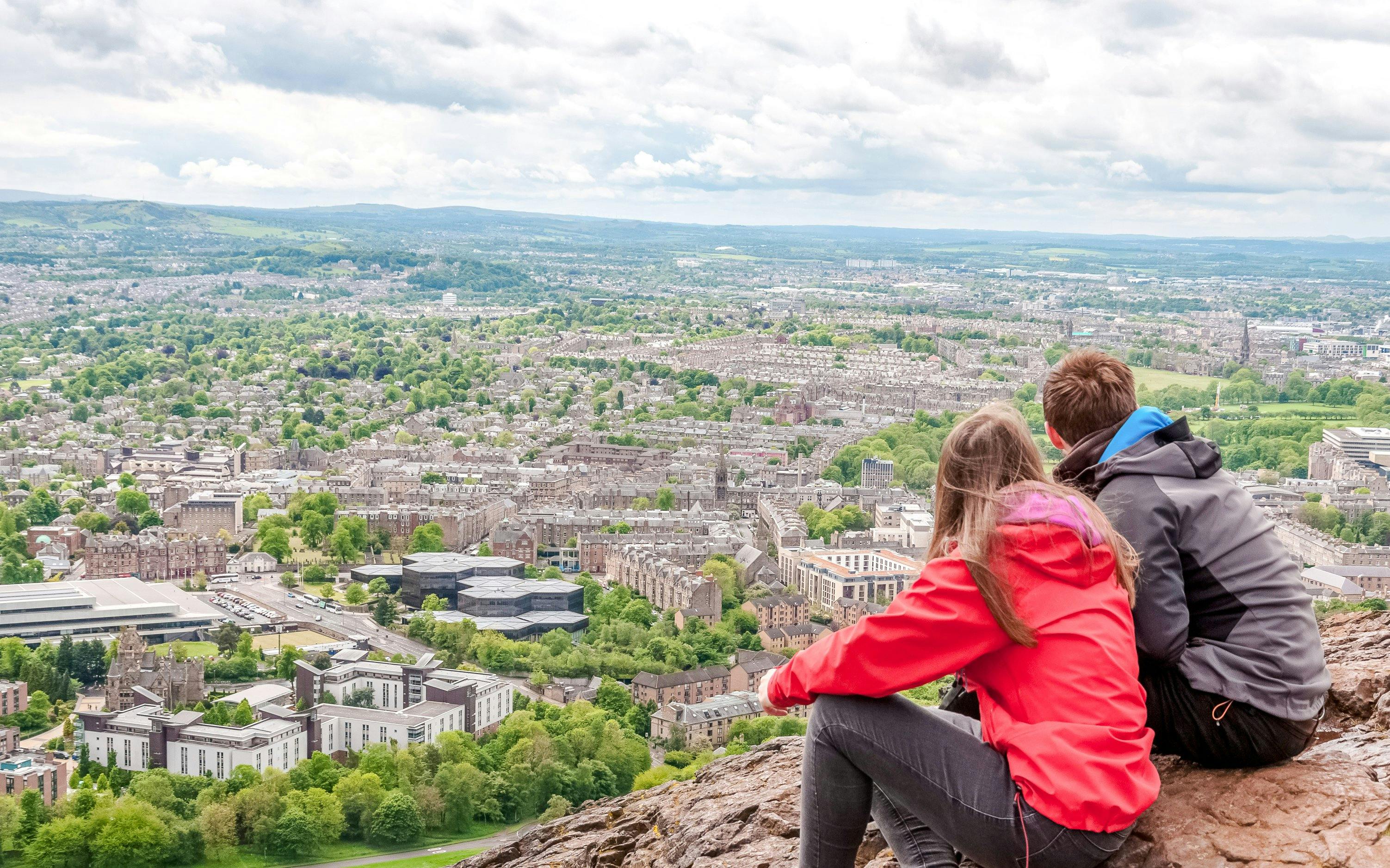 Couple overlooking Edinburgh cityscape from Arthur's Seat near Holyrood Abbey.