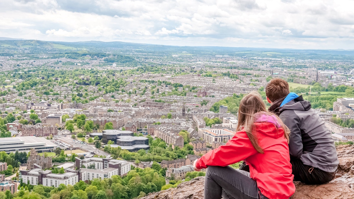 Couple overlooking Edinburgh cityscape from Arthur's Seat near Holyrood Abbey.