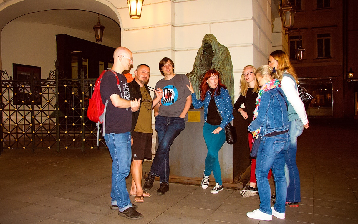 Group of tourists on a Ghosts and Legends of Prague tour near a cloaked statue.