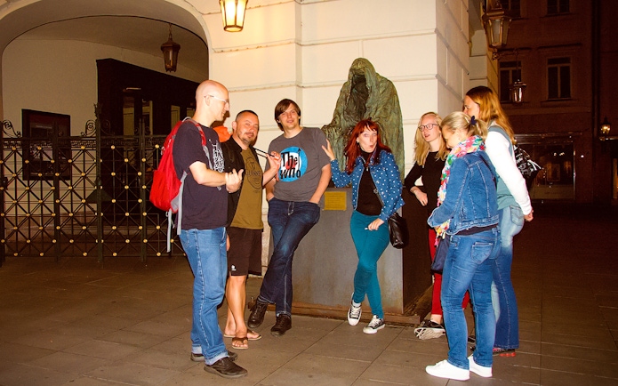 Group of tourists on a Ghosts and Legends of Prague tour near a cloaked statue.