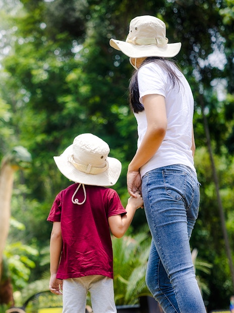 Mom and child viewing dinosaur models in a lush park setting.