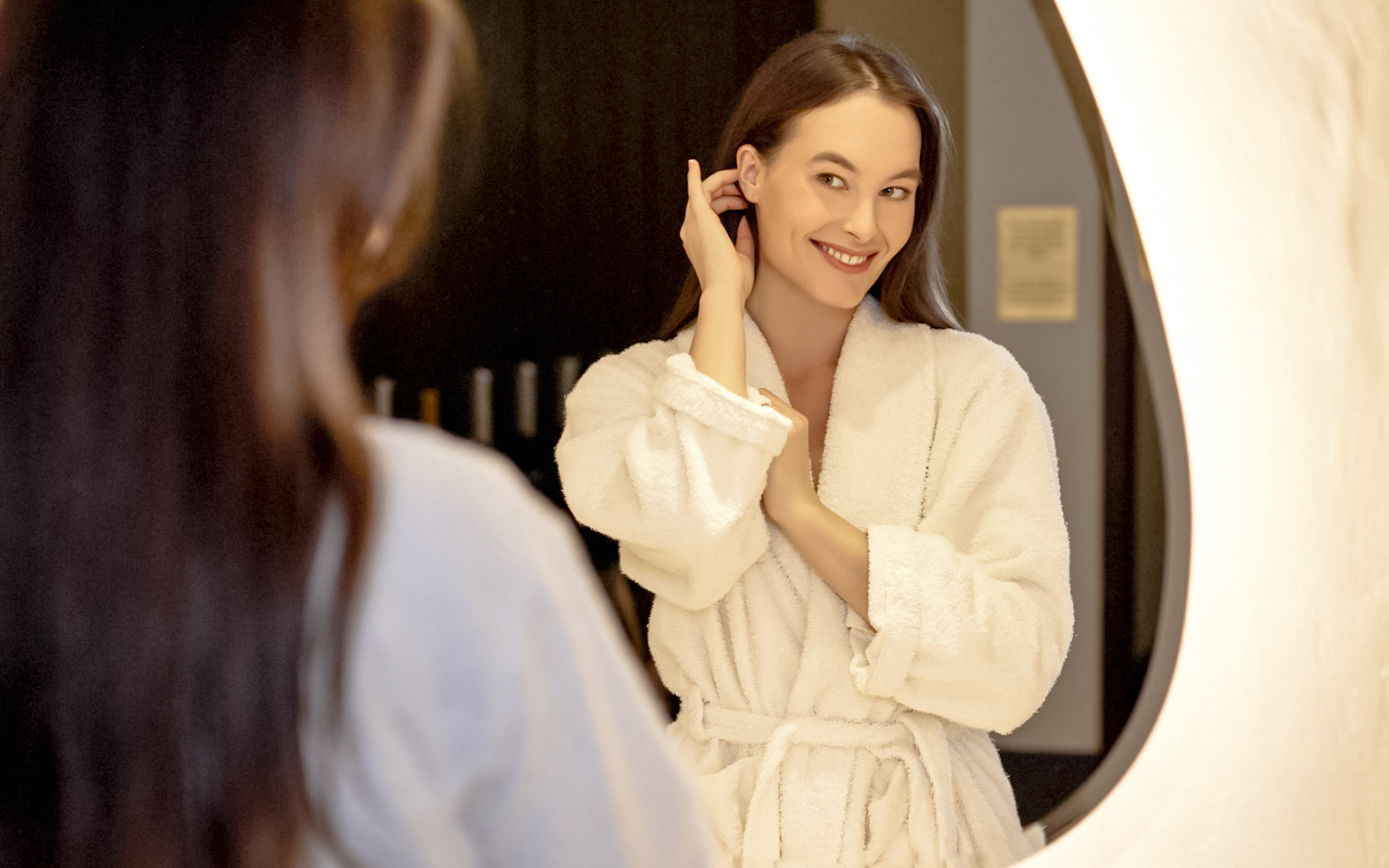 Person in a robe smiling in front of a mirror at Mandala Day Spa.