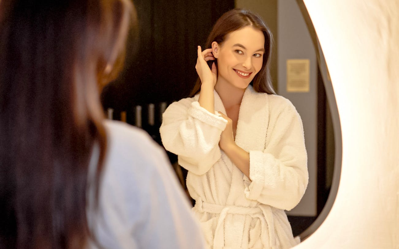 Person in a robe smiling in front of a mirror at Mandala Day Spa.