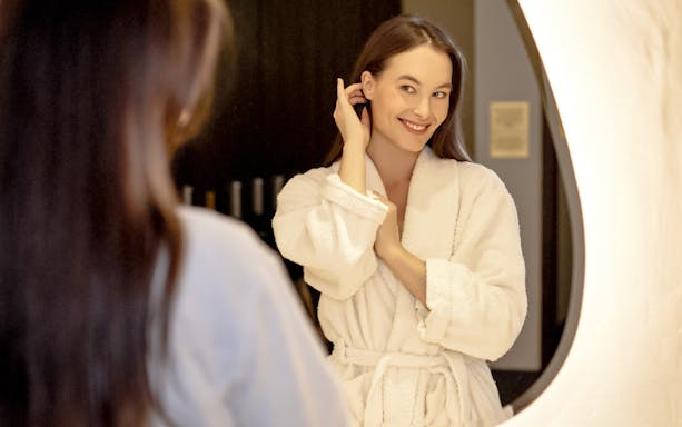 Person in a robe smiling in front of a mirror at Mandala Day Spa.