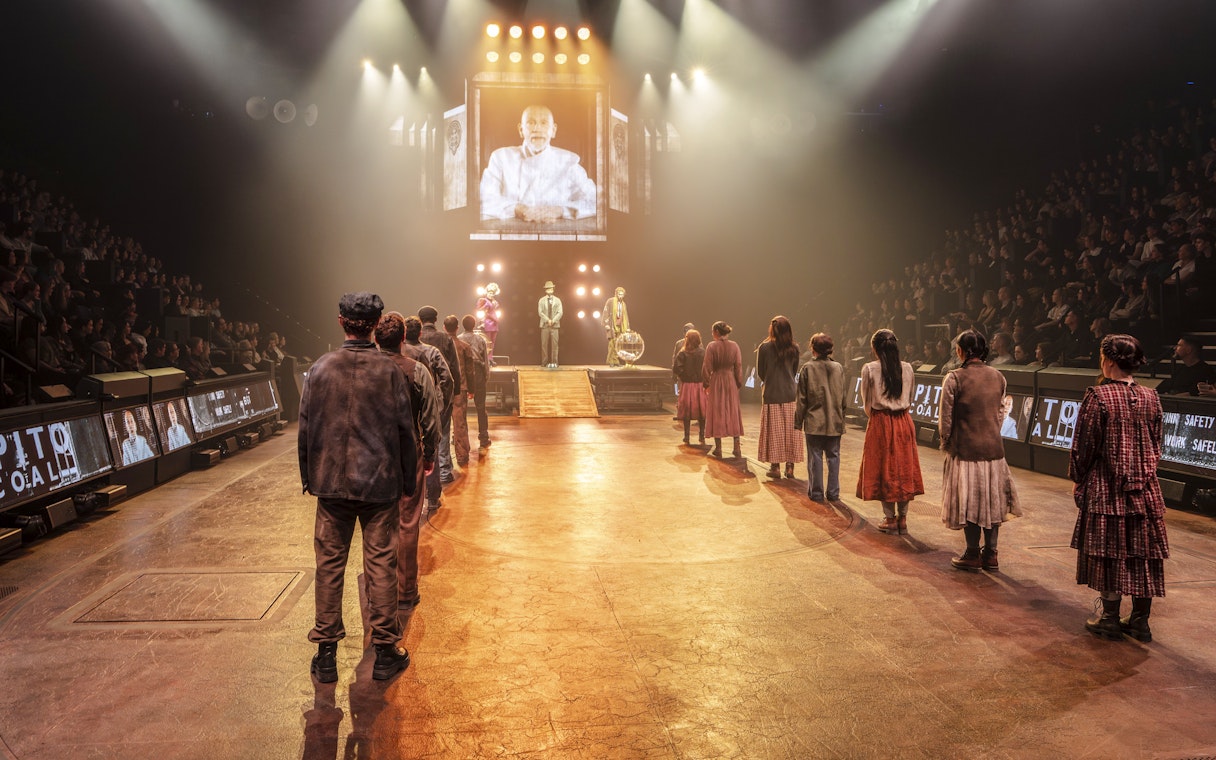 Hunger Games West End show stage performance with actors in line facing a large screen.