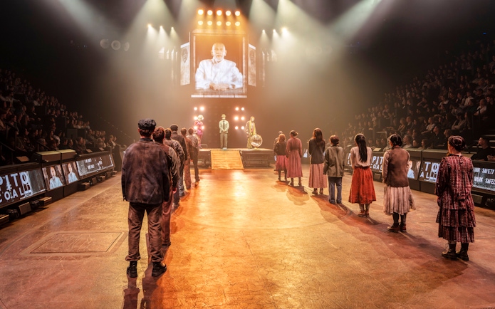 Hunger Games West End show stage performance with actors in line facing a large screen.