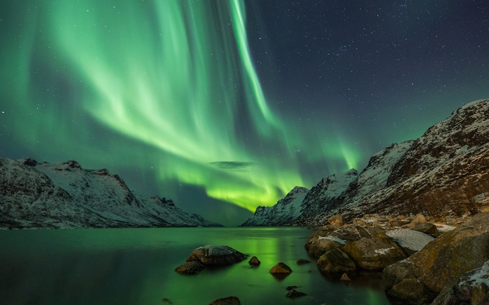 Northern lights over snowy mountains and a lake in Tromso.