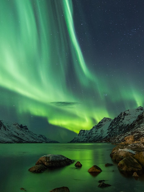 Northern lights over snowy mountains and a lake in Tromso.