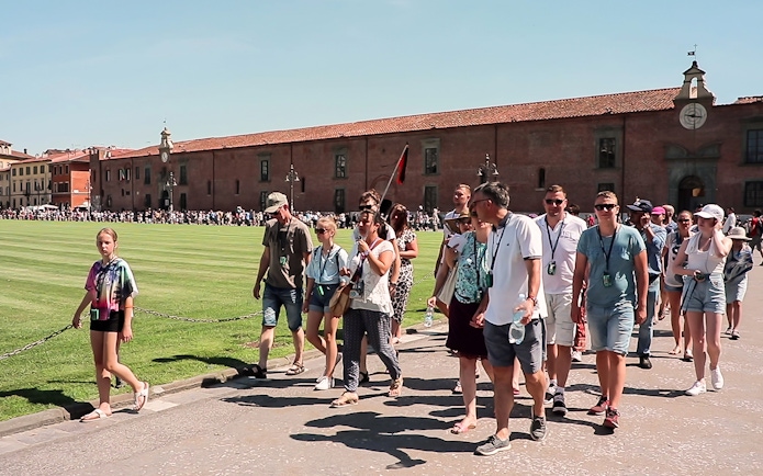 Tour group walking in Pisa with a guide holding a flag, part of a guided tour from Florence.