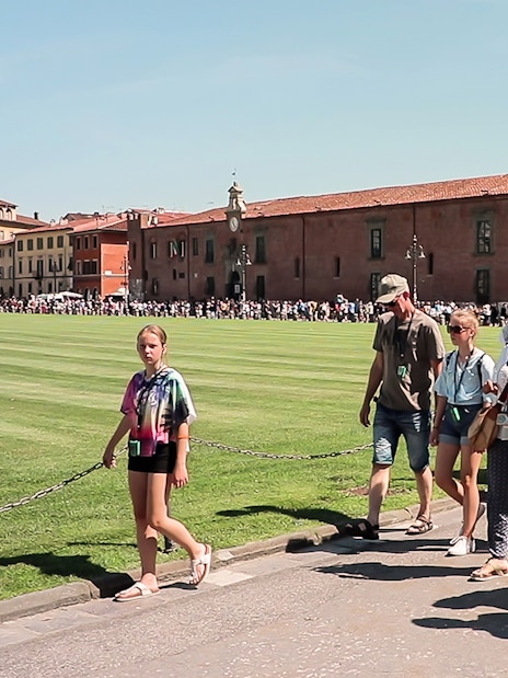 Tour group walking in Pisa with a guide holding a flag, part of a guided tour from Florence.