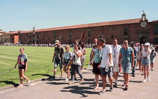 Tour group walking in Pisa with a guide holding a flag, part of a guided tour from Florence.